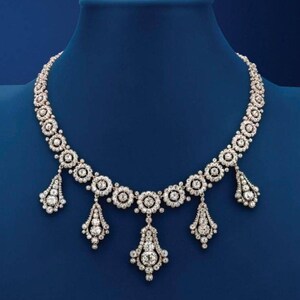 May include: A diamond necklace with a central row of round diamond clusters and three dangling teardrop-shaped diamond clusters.