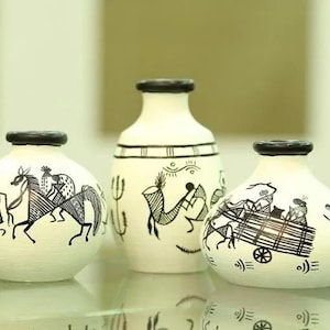 Könnte beinhalten: Drei weiße Keramikvasen mit schwarzen Stammeskunst-Designs. Die Vasen haben schwarze Ränder und zeigen Illustrationen von Menschen, Pferden und Karren. Die Vasen sind auf einer reflektierenden Oberfläche angeordnet.