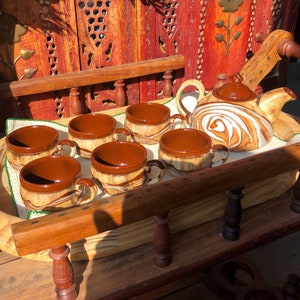 May include: A set of six brown and white ceramic teacups and a matching teapot with a swirling white design on a wooden tray.