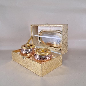 Op de afbeelding: Een goudkleurige decoratieve doos met een getextureerde afwerking, met twee koperkleurige wierookbranders met gouden deksels. De doos bevat ook een zilverkleurig dienblad met een witte stok. De set is ontworpen voor het branden van wierook.