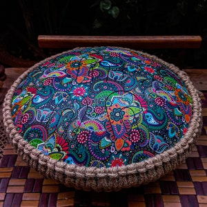 May include: A colourful hand drum with a paisley pattern and a brown rope border. The drum is made of wood and has a round shape.