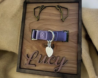 May include: A wooden plaque with a cutout of a dog's head, a purple dog collar, a silver heart-shaped tag, and the name "Lucy" engraved in cursive.