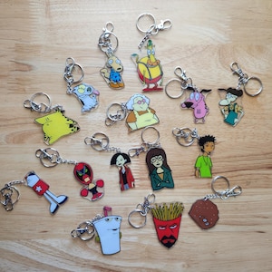 May include: A collection of cartoon character keychains with silver key rings. The keychains feature various characters in bright colors, including a pink dog, a yellow character, and a red-faced character with fries.