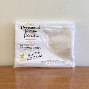 Può includere: Un pacchetto bianco contenente un lenzuolo piatto di dimensioni standard realizzato in 50% poliestere e 50% cotone pettinato. La confezione è etichettata "Permanent Press Percale" e "Selected Irregulars".