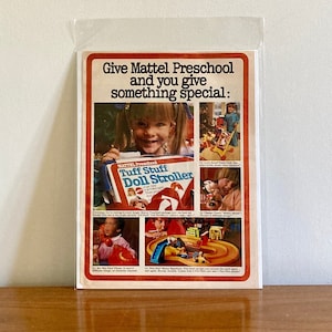 May include: A vintage advertisement for Mattel Preschool toys. The ad features a young girl holding a doll stroller and the text "Give Mattel Preschool and you give something special."