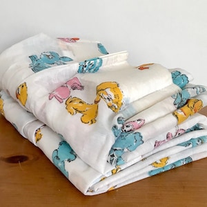 May include: A stack of white cotton sheets with a colorful cartoon animal print. The print features blue, yellow, pink, and orange animals.