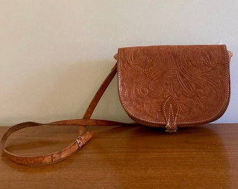 Peut inclure: Un sac à bandoulière en cuir marron avec un motif floral en relief. Le sac a une longue bandoulière et une fermeture à rabat.