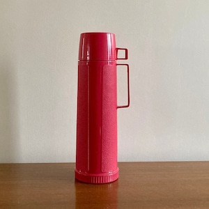 May include: A pink plastic thermos with a textured surface and a handle.