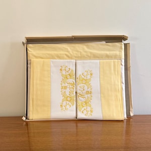 May include: A set of two yellow pillowcases with white embroidered trim and the word "Happy" in gold lettering.