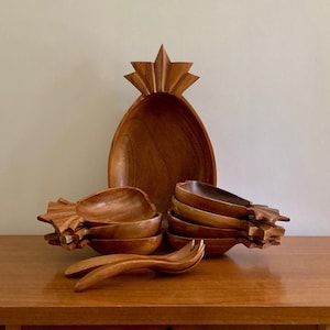 May include: A set of wooden pineapple-shaped bowls, including a large serving bowl and smaller individual bowls. The bowls are made of dark brown wood and have a natural, rustic finish.