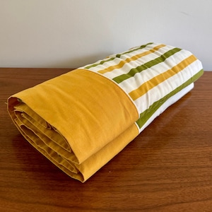May include: A folded yellow and green striped bed sheet with a solid yellow border.