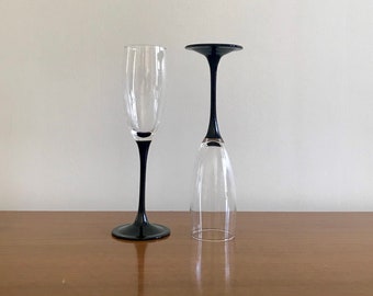 May include: Two champagne flutes with black stems. One flute is filled with liquid, the other is empty.