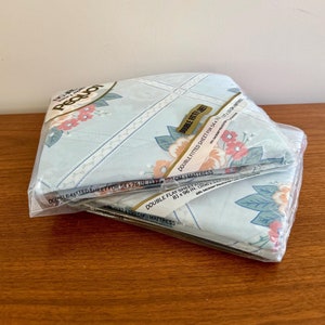 Könnte beinhalten: Zwei Packungen mit blauen und weißen Bettwäsche mit Blumenmuster. Das Etikett auf der Verpackung lautet "Doppel-Spannbettlaken für 54 x 76 Zoll (137 x 193 cm) Matratze" und "Doppel-Flachbettlaken 81 x 96 Zoll (205 x 244 cm) Matratze".