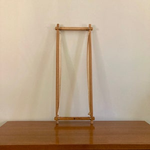 Puede incluir: Un aro de bordado de madera con una tela blanca estirada sobre él. El aro está sobre una mesa de madera.