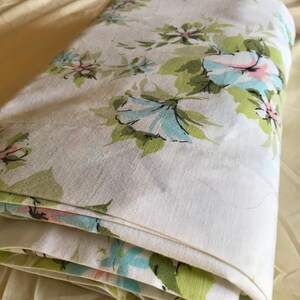 Puede incluir: Una s&aacute;bana de tela blanca con un patr&oacute;n floral en tonos de verde, azul y rosa. La s&aacute;bana est&aacute; doblada y tiene una superficie suave y texturizada.