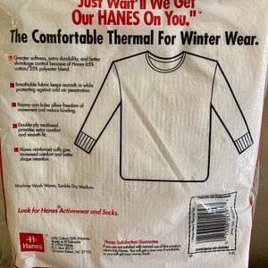 Peut inclure: Un haut thermique blanc &agrave; manches longues et col rond. L'emballage pr&eacute;sente le texte "Just Wait'll We Get Our HANES On You." et "The Comfortable Thermal For Winter Wear." L'emballage comprend &eacute;galement une description des caract&eacute;ristiques du produit, telles que son tissu respirant, ses emmanchures amples et son col double &eacute;paisseur.