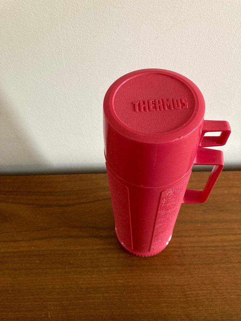 May include: A pink thermos with a handle and the word "THERMOS" embossed on the lid.