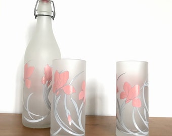 May include: Two frosted glass tumblers with pink floral designs and a frosted glass bottle with a silver metal swing top lid. The bottle and glasses have a pink floral design.