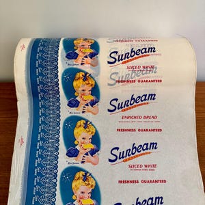 Puede incluir: Rollo de envoltorio de pan Sunbeam vintage. El diseño incluye una niña comiendo pan, el logotipo de Sunbeam y el texto «Sliced White» y «Enriched Bread». El envoltorio es blanco y azul.