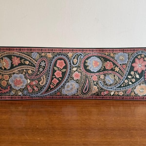 May include: A paisley patterned wallpaper border with pink, blue, and gold accents on a black background.