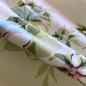 Puede incluir: Primer plano de una tela blanca con un patr&oacute;n floral verde y azul. La tela est&aacute; doblada y el patr&oacute;n es visible en ambos lados del pliegue.