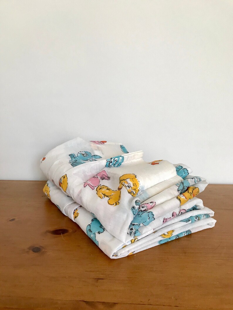 May include: A stack of white cotton sheets with a colorful cartoon animal print. The print features blue, yellow, pink, and orange animals.