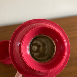 May include: Close-up of the inside of a red thermos bottle. The lid is off and the inside of the bottle is visible. The bottle is made of metal and has a shiny finish.
