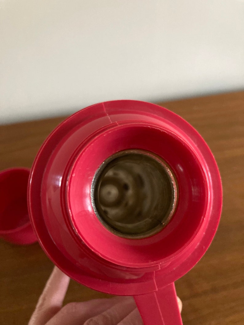 May include: Close-up of the inside of a red thermos bottle. The lid is off and the inside of the bottle is visible. The bottle is made of metal and has a shiny finish.