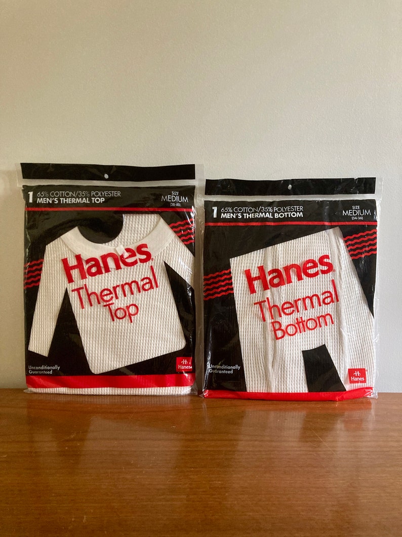 Peut inclure: Deux paquets de sous-v&ecirc;tements thermiques blancs, un haut et un bas, tous deux &eacute;tiquet&eacute;s "Hanes Thermal" en lettres rouges. Les paquets sont tous deux de taille moyenne et sont faits de 65% de coton et 35% de polyester.