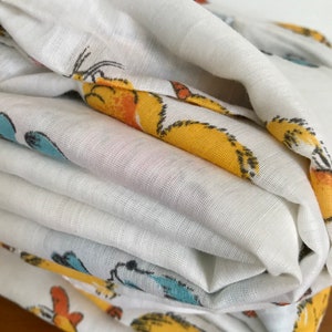 May include: A stack of white fabric with a yellow, orange, and blue cartoon animal print. The fabric is folded neatly and the print is visible on the top and bottom layers.