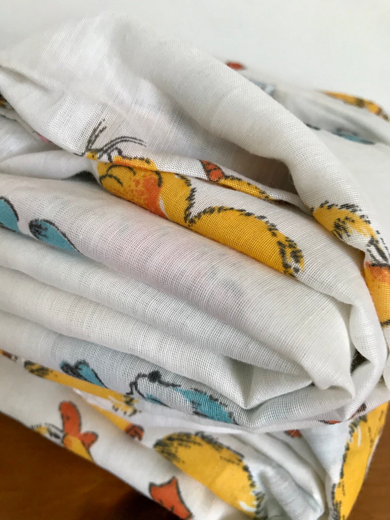May include: A stack of white fabric with a yellow, orange, and blue cartoon animal print. The fabric is folded neatly and the print is visible on the top and bottom layers.
