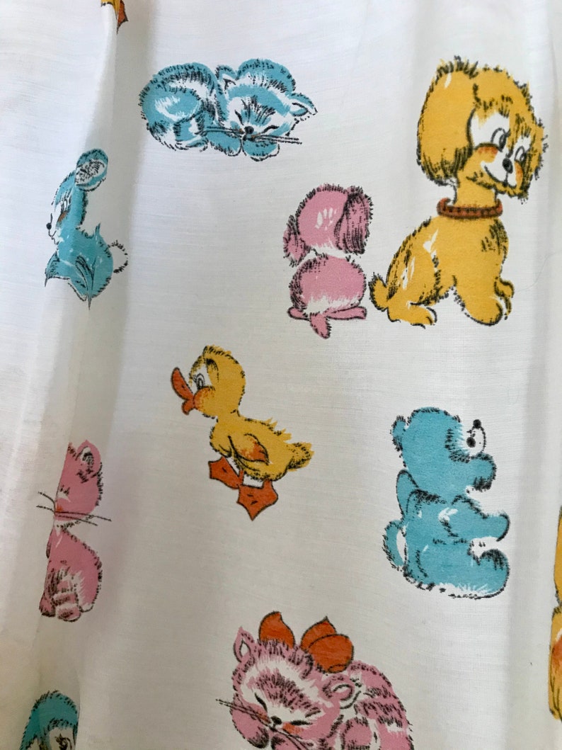 May include: White fabric with a repeating pattern of cartoon animals. The animals include a duck, a cat, a dog, a bear, and a rabbit. The animals are all in different colors, including blue, yellow, pink, and brown.