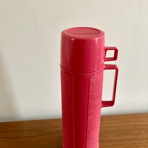 May include: A pink Thermos brand vacuum insulated bottle with a textured surface and a carrying handle.