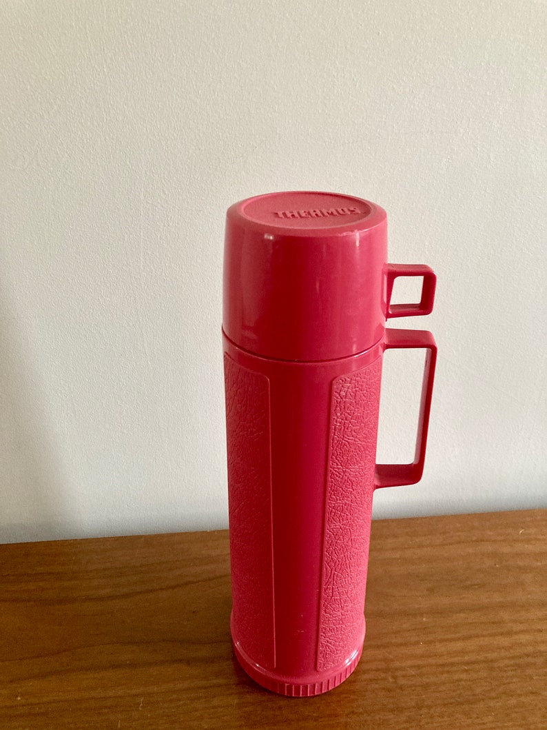 May include: A pink Thermos brand vacuum insulated bottle with a textured surface and a carrying handle.