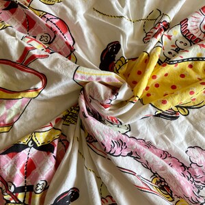 May include: White fabric with a repeating pattern of clowns in pink, yellow, and red. The clowns are wearing hats and holding various objects. The fabric is crumpled and folded.