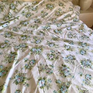 Puede incluir: S&aacute;banas blancas de cama con un patr&oacute;n floral con flores azules y rosas sobre un fondo blanco.