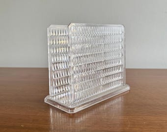 Op de afbeelding: Een transparante servetthouder van plastic met een ruitpatroon.