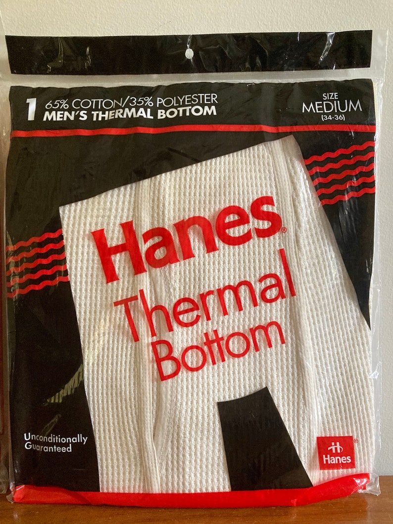 Peut inclure: Emballage de sous-v&ecirc;tements thermiques blancs avec du texte rouge et noir qui indique "Hanes Thermal Bottom" et "65% Coton/35% Polyester". L'emballage comprend &eacute;galement la taille "Medium (34-36)" et le texte "Garantie inconditionnelle".