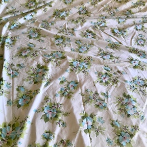 Puede incluir: S&aacute;bana blanca de cama con un patr&oacute;n floral con flores azules y rosas sobre tallos verdes. La s&aacute;bana est&aacute; arrugada y tiene un aspecto vintage.