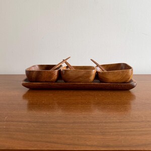 May include: A set of three wooden bowls with matching spoons, all resting on a wooden tray. The bowls and tray are a rich brown colour.