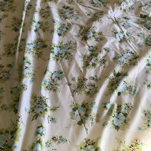 Puede incluir: Tela blanca con un patr&oacute;n floral con flores azules y rosas sobre tallos verdes. La tela est&aacute; arrugada y tiene un aspecto vintage.