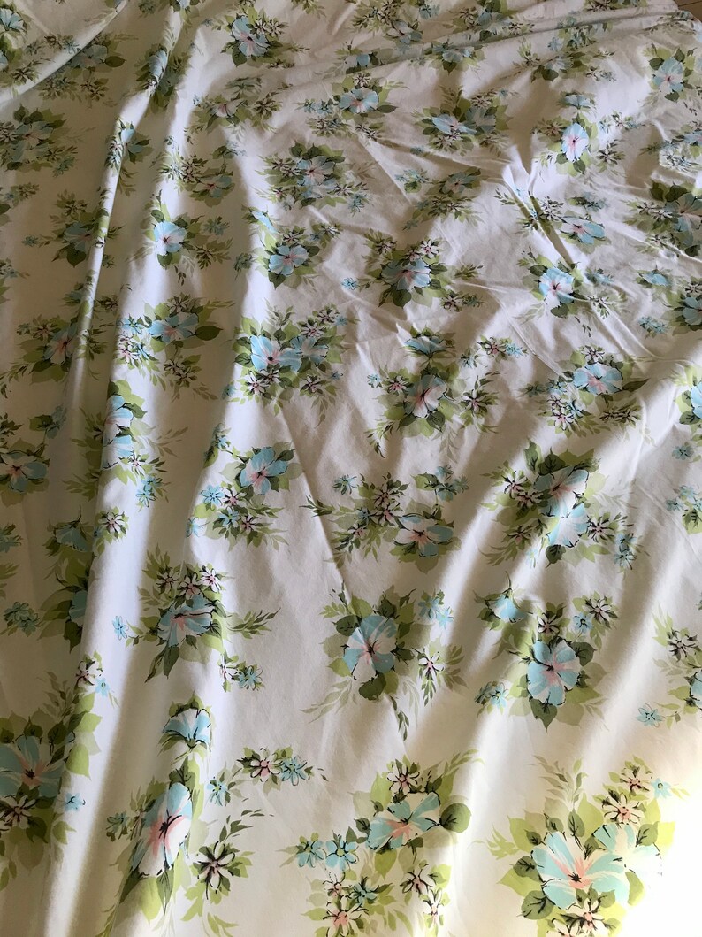 Puede incluir: Tela blanca con un patr&oacute;n floral con flores azules y rosas sobre tallos verdes. La tela est&aacute; arrugada y tiene un aspecto vintage.