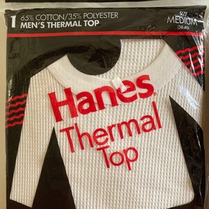 Peut inclure: Un haut thermique blanc &agrave; manches longues avec une texture en nid d'abeille. L'&eacute;tiquette indique "Hanes Thermal Top" en lettres rouges. L'emballage indique &eacute;galement "65% Coton/35% Polyester Haut Thermique Homme" et "Taille M (38-40)".