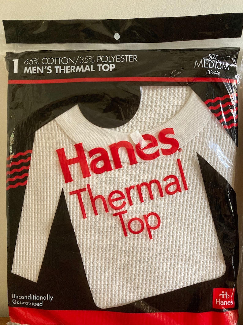 Peut inclure: Un haut thermique blanc &agrave; manches longues avec une texture en nid d'abeille. L'&eacute;tiquette indique "Hanes Thermal Top" en lettres rouges. L'emballage indique &eacute;galement "65% Coton/35% Polyester Haut Thermique Homme" et "Taille M (38-40)".
