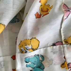 May include: White fabric with a repeating pattern of cartoon ducks and bears. The ducks are yellow with orange beaks and feet. The bears are blue, pink, and yellow.