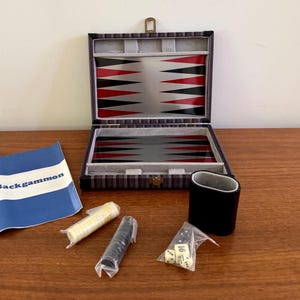 May include: Open backgammon set with a striped case, red and black triangles, and a gray playing surface. Includes dice, game pieces, and a black cup. The game pieces are yellow and black.
