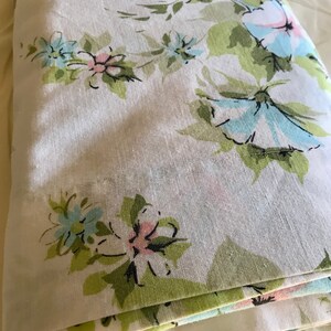Puede incluir: Una tela blanca doblada con un patr&oacute;n floral en tonos verdes, azules y rosas. Las flores son estilizadas y tienen un aspecto vintage.