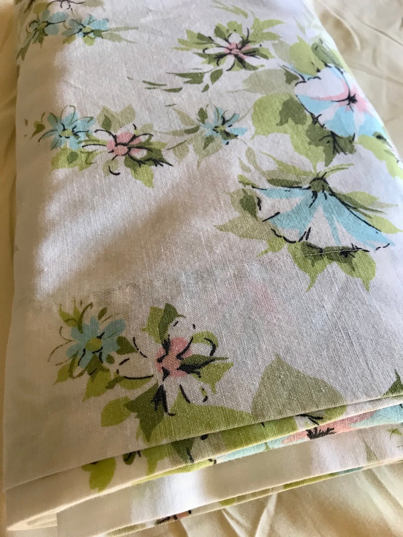 Puede incluir: Una tela blanca doblada con un patr&oacute;n floral en tonos verdes, azules y rosas. Las flores son estilizadas y tienen un aspecto vintage.