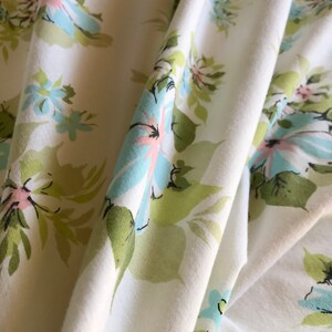 Puede incluir: Tela blanca con un patr&oacute;n floral con flores de color azul claro, rosa y verde. La tela est&aacute; doblada y drapeada, mostrando el patr&oacute;n.