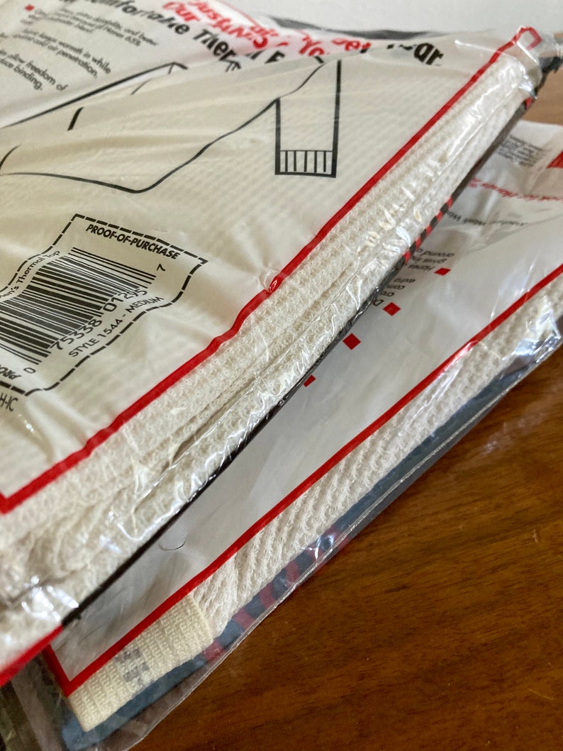 Peut inclure: Sous-v&ecirc;tements thermiques blancs emball&eacute;s dans un sac en plastique transparent avec une &eacute;tiquette rouge et blanche. L'&eacute;tiquette indique "Preuve d'achat" et comporte un code-barres. L'&eacute;tiquette indique &eacute;galement "Style 1544 - Medium".